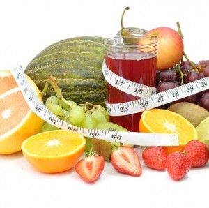 Fresh glass of juice surrounded by an assortment of fruit and a tape measure